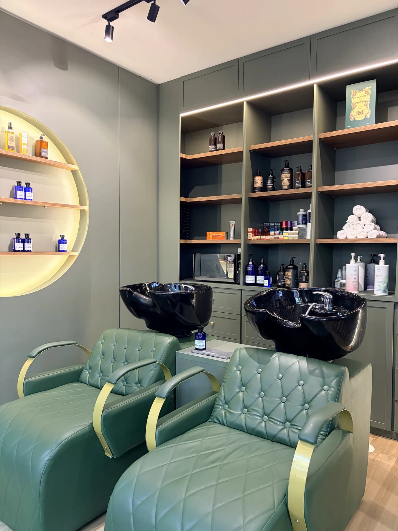 Espaço de lavatórios com poltronas capitonê verdes e produtos selecionados